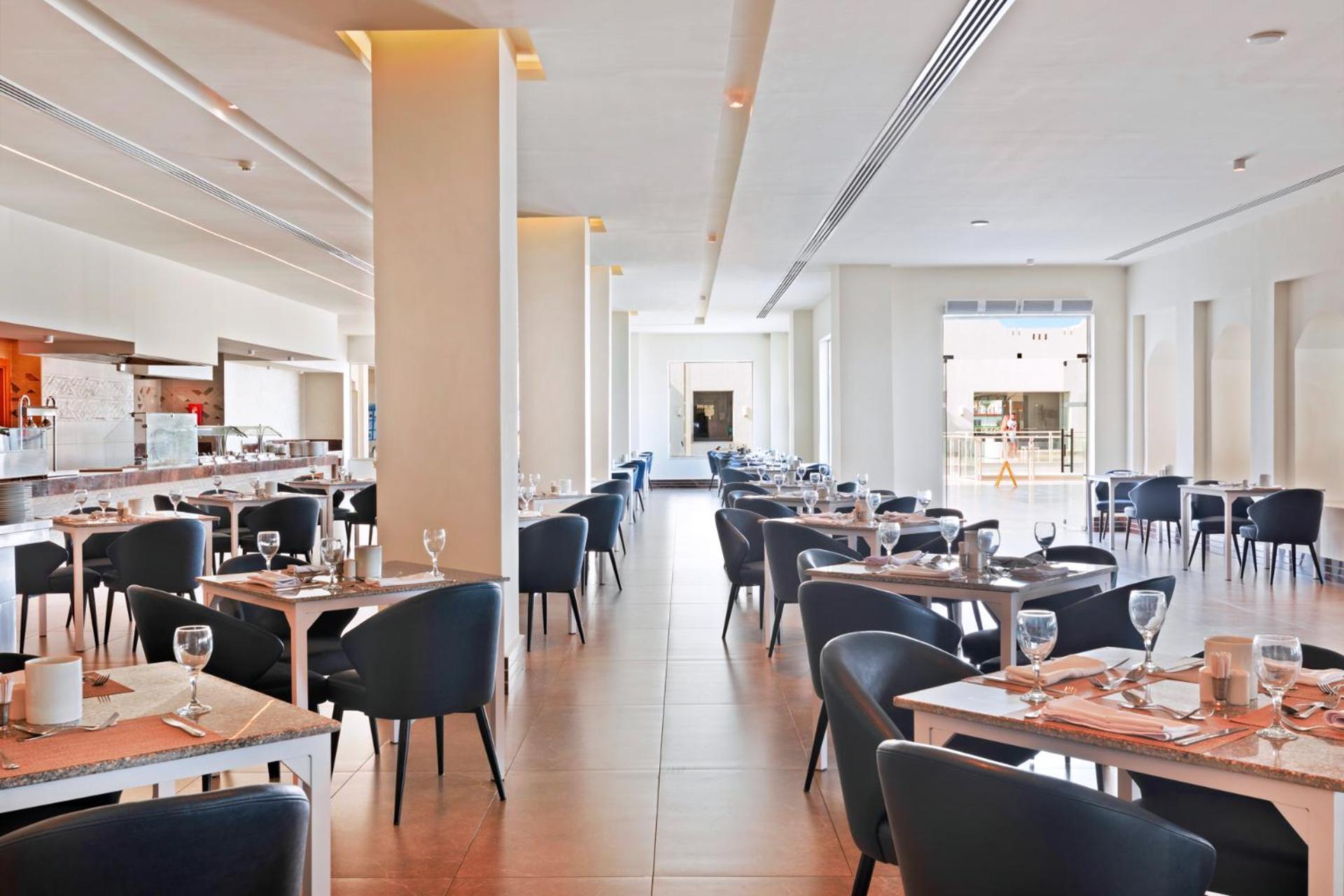 Pickalbatros Royal Grand Sharm - Adults Friendly 16 Years Plus Luaran gambar The photo shows the interior of a modern restaurant. The space is bright and airy, featuring large windows that allow natural light to flood in. There are several tables arranged throughout the room, each covered with placemats and set with glasses a