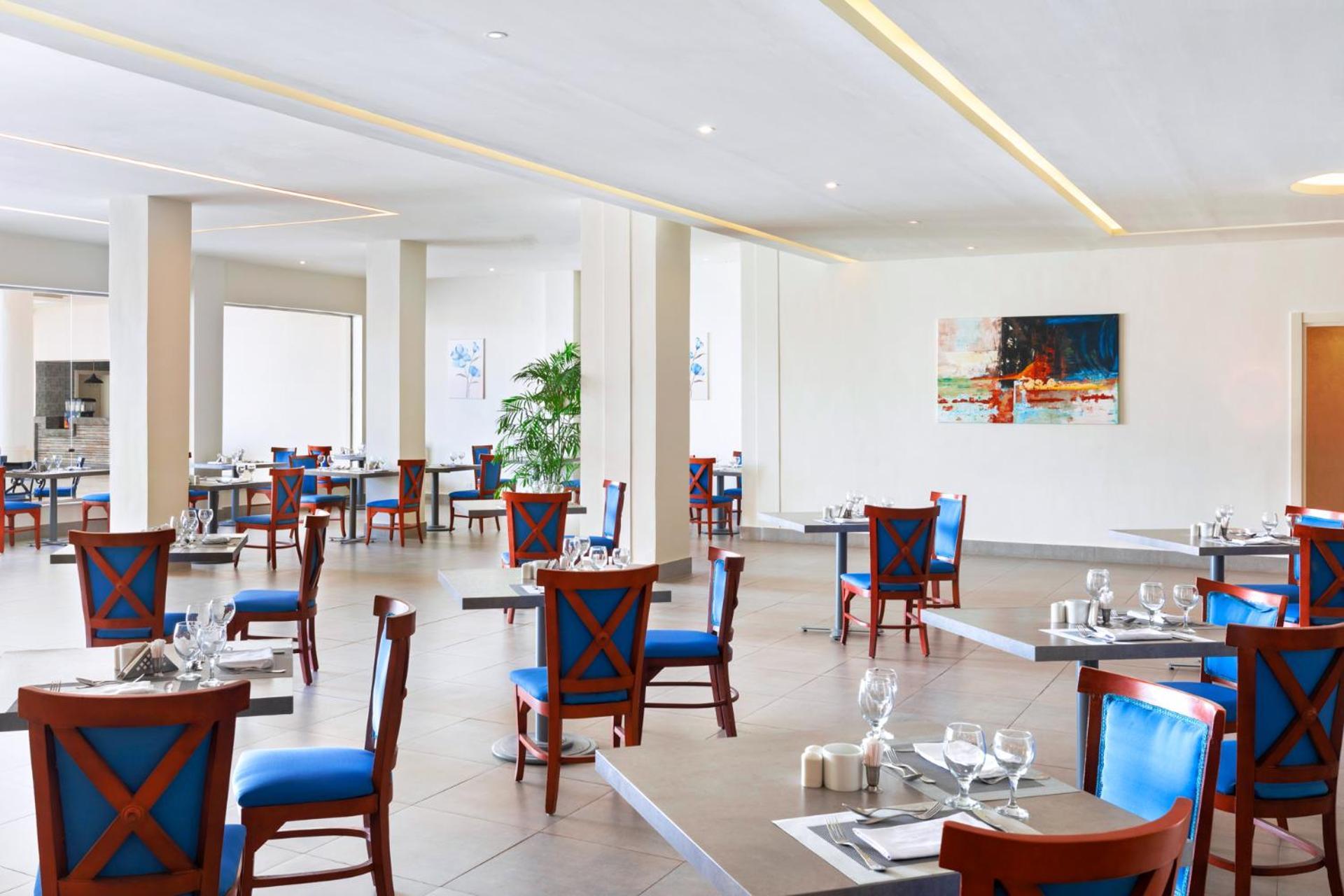Pickalbatros Royal Grand Sharm - Adults Friendly 16 Years Plus Luaran gambar The photo shows an interior of a restaurant featuring a modern and spacious design. The floors are tiled, and the walls are painted in neutral tones. The seating consists of wooden chairs with blue cushions arranged around tables, which are set with 