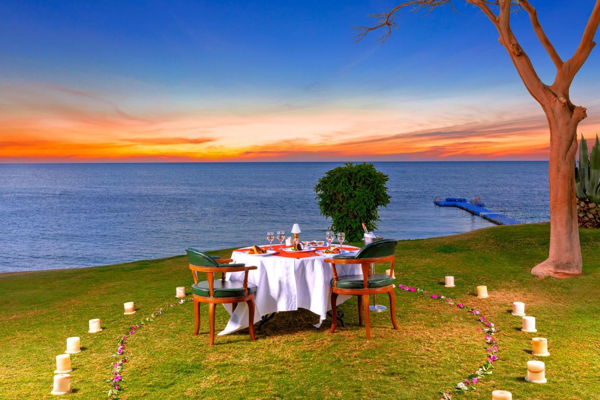 Pickalbatros Royal Grand Sharm - Adults Friendly 16 Years Plus Luaran gambar The photo depicts a romantic outdoor dining setup by the seaside. In the foreground, there is a round table elegantly set with a white tablecloth, plates, and glassware, creating a cozy atmosphere. Surrounding the table are green chairs. A circle of 