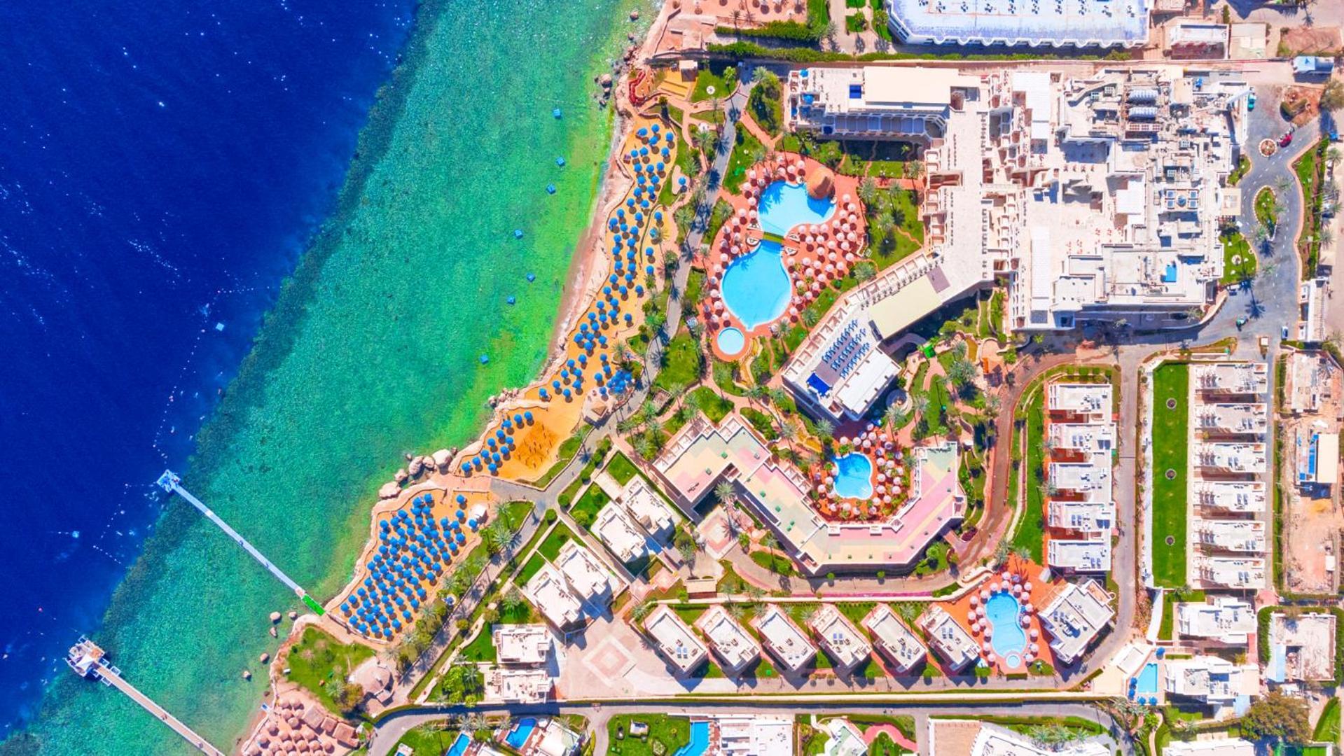 Pickalbatros Royal Grand Sharm - Adults Friendly 16 Years Plus Luaran gambar The image shows an aerial view of a coastal resort area. It features various swimming pools outlined by landscaped gardens and pathways. There are also rows of sun loungers and umbrellas near the beach. The water transitions from a deep blue to a vib