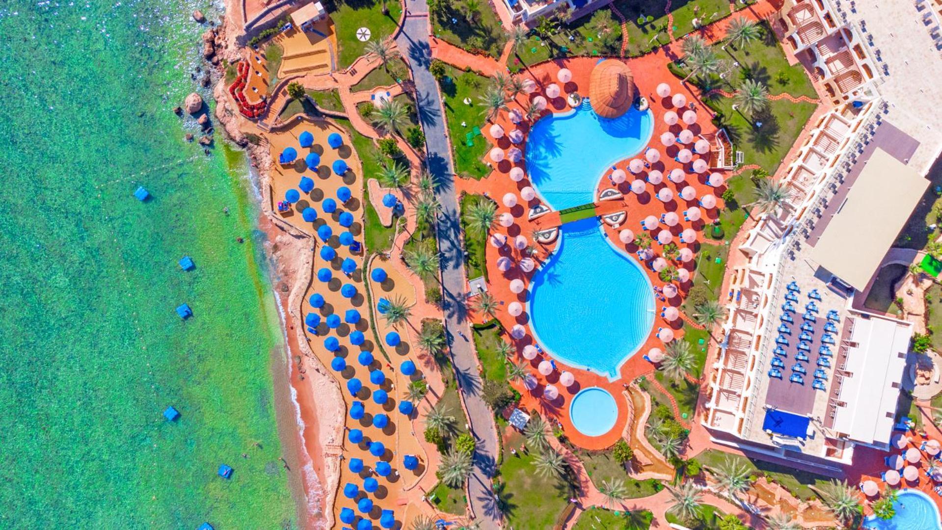 Pickalbatros Royal Grand Sharm - Adults Friendly 16 Years Plus Luaran gambar The photo shows an aerial view of a beach resort. In the foreground, there's a large swimming pool shaped like a flowing river, surrounded by lounge chairs and umbrellas. The pool has a distinctive, organic design with curved edges. To the left, ther