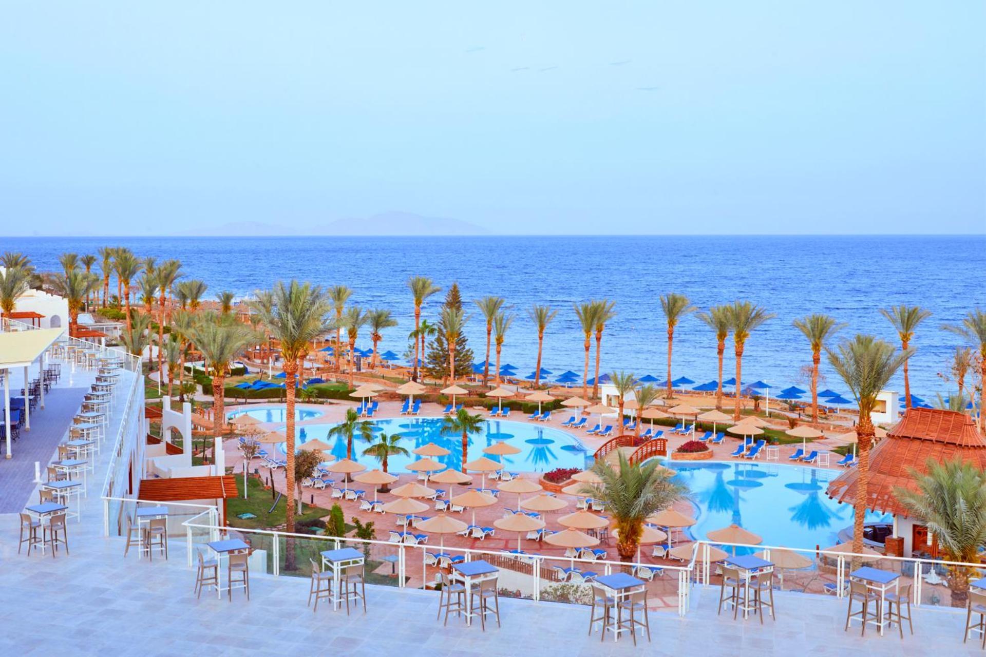 Pickalbatros Royal Grand Sharm - Adults Friendly 16 Years Plus Luaran gambar The photo depicts a scenic resort area by the sea. In the foreground, there is a large swimming pool surrounded by lounge chairs and umbrellas. Palm trees line the sides of the pool, adding to the tropical atmosphere. In the background, a beautiful b